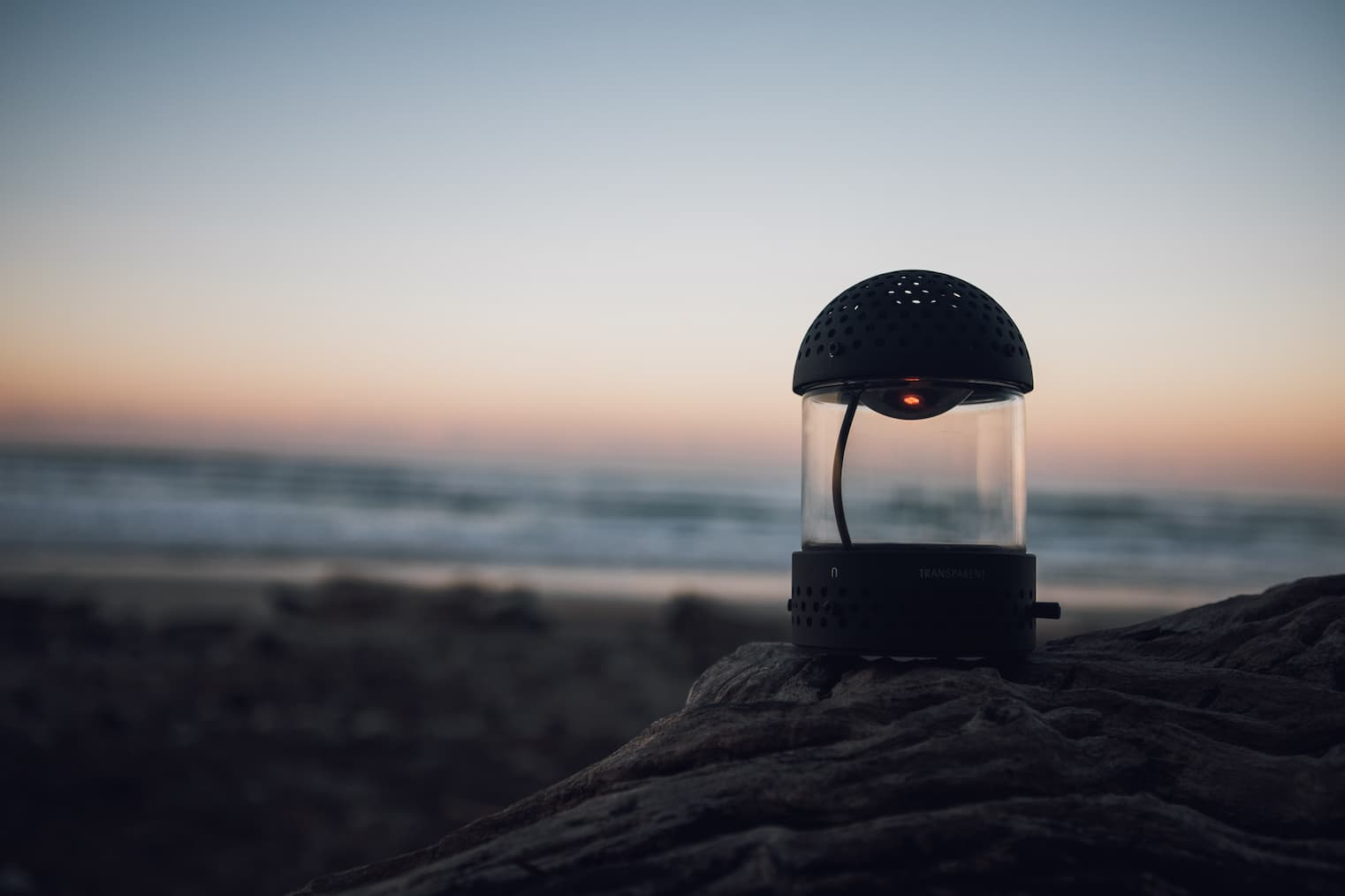 Transparent Light Speaker in Black on a beach at dawn
