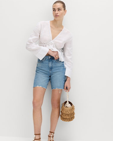 Woman wearing a White Pure Linen V-Neck Peplum Top and Light Indigo Denim Barrel Raw Hem Mid Rise Shorts