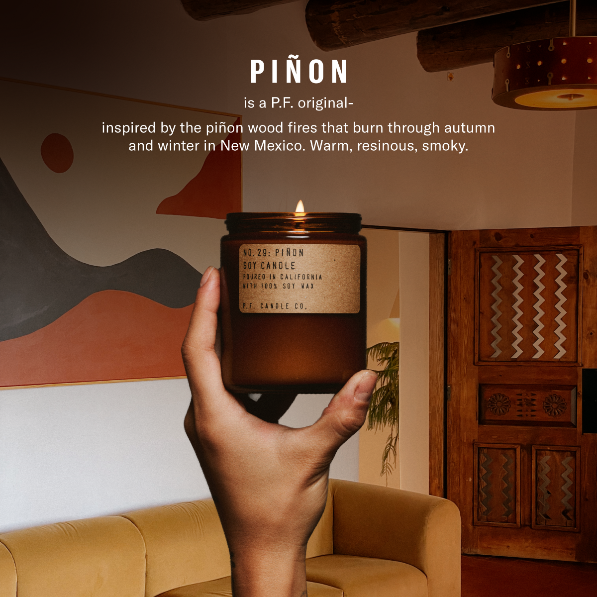 Piñon is a P.F. original — inspired by the piñon wood fires that burn through autumn and winter in New Mexico. Warm, resinous, smoky.  [hand holding lit candle in front of bookcase]
