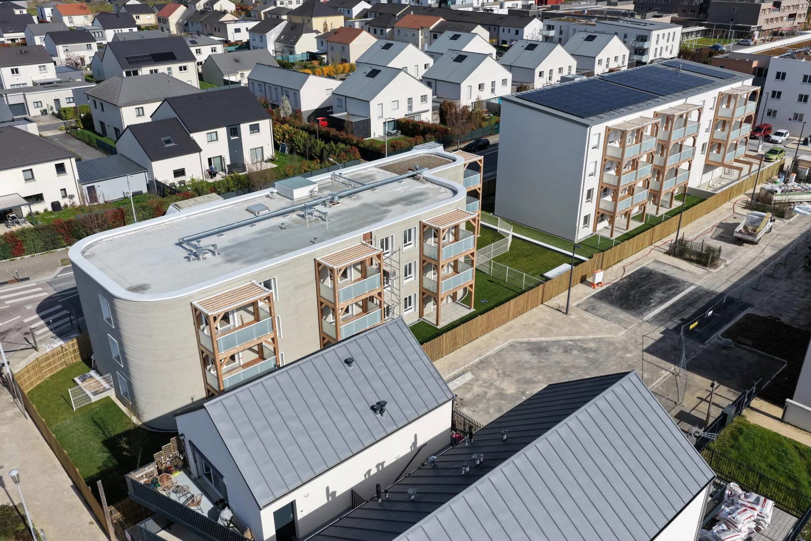 Aerial view of a 3D printed building next to a nearly identical traditional built one