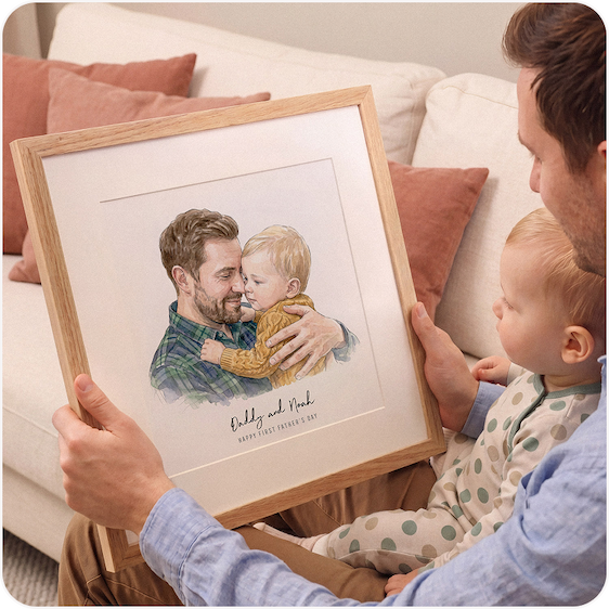 A father holding a framed watercolour illustration of himself with his young child, with a baby beside them