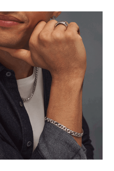 Close-up of male model wearing a thick silver chain, silver bracelet, signet ring and diamond stud earring.