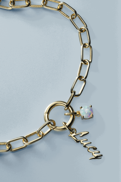 Yellow gold paperclip chain bracelet with script letter charm and opal gemstone accent.