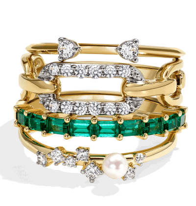 Stacked yellow gold rings with emerald gemstones, diamonds, and pearl accents.