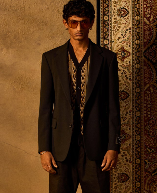 Mann in schwarzem Anzug, kombiniert mit gemustertem Stricktop in Schwarz und Beige sowie Sonnenbrille