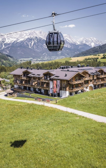 Gondel im Vordergrund des Hotel sowie einer Bergkette im Sommer