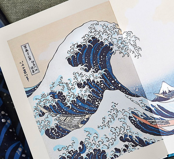 Open book featuring Hokusai’s iconic wave motif, The Great Wave off Kanagawa. - Shop Inspired by Hokusai.