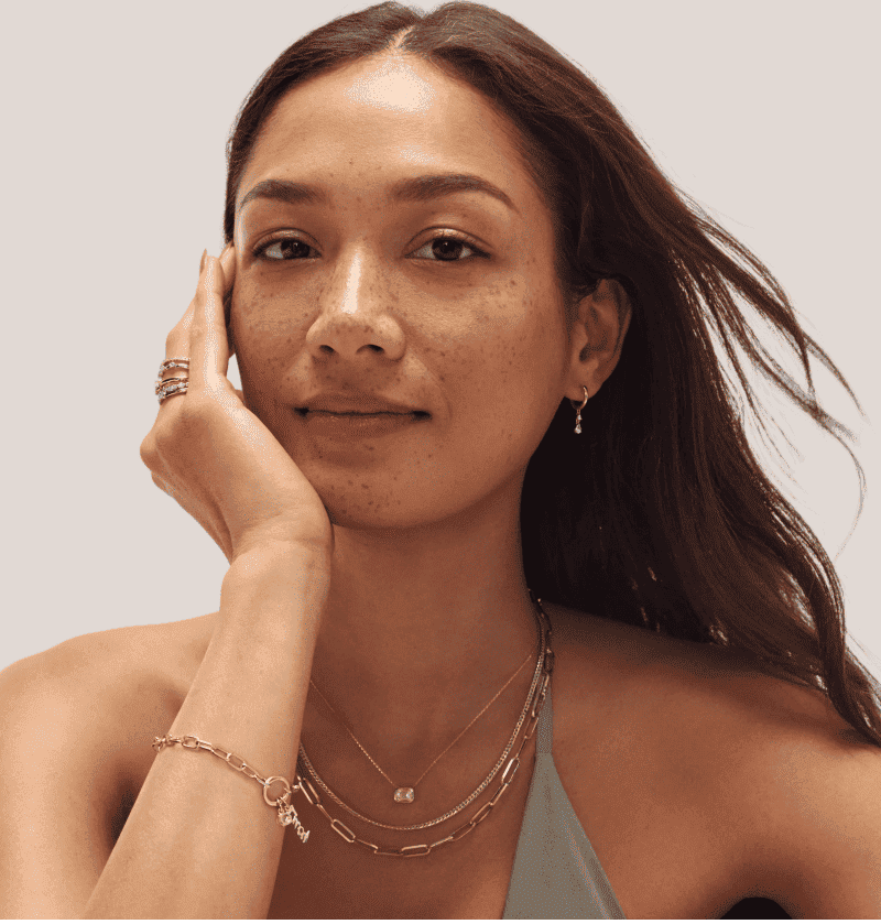 Woman wearing various yellow gold jewelry, including rings, chains, a bracelet and earrings.