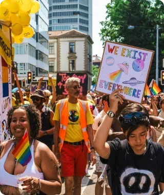 Person holding a sign at a sunny city Pride parade.