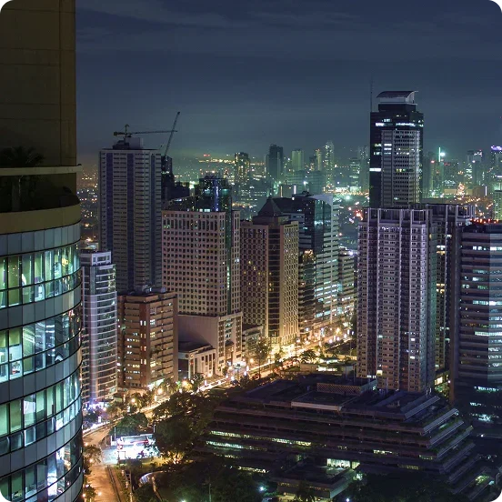 A high-angle night view of a dense city skyline with illuminated skyscrapers and busy streets.