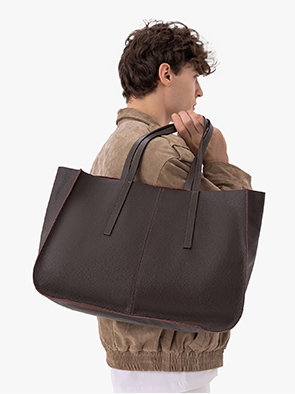 Man in brown jacket holding large dark brown leather tote bag on shoulder.