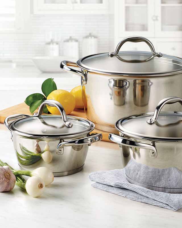 Three shiny stainless steel pots with lids, surrounded by lemons and onions on a kitchen countertop.