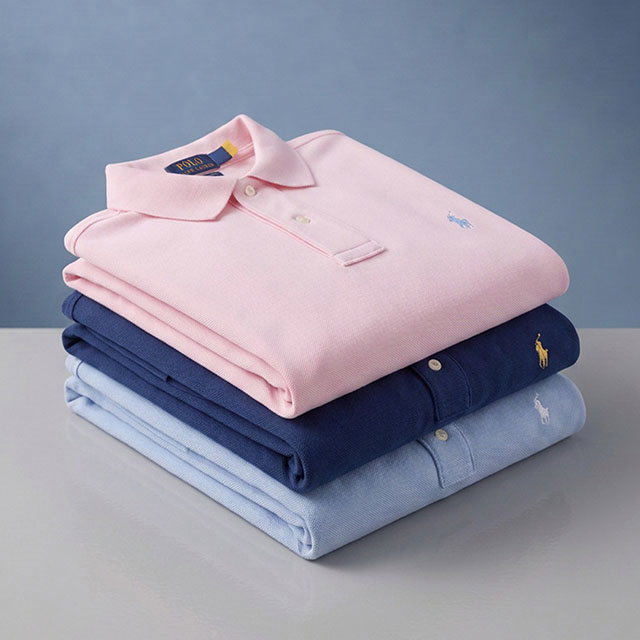 A stack of three folded polo shirts in pastel pink, navy blue, and light blue, each with a small embroidered logo.