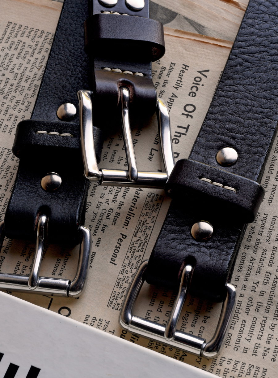 Three Bills Khakis belts lay along vintage newspapers