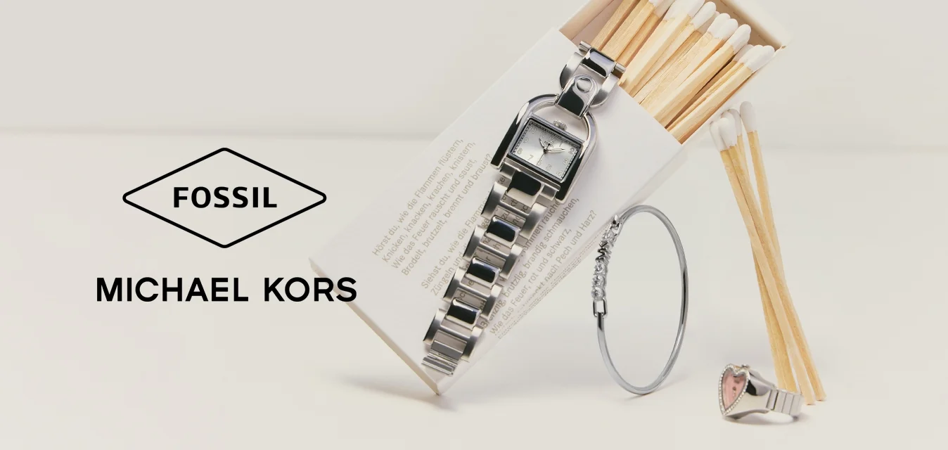 Eine Metallarmbanduhr, ein silbernes Armband und ein Ring ruhen an einer offenen Streichholzschachtel mit Holzstreichhölzern auf einer weißen Oberfläche.