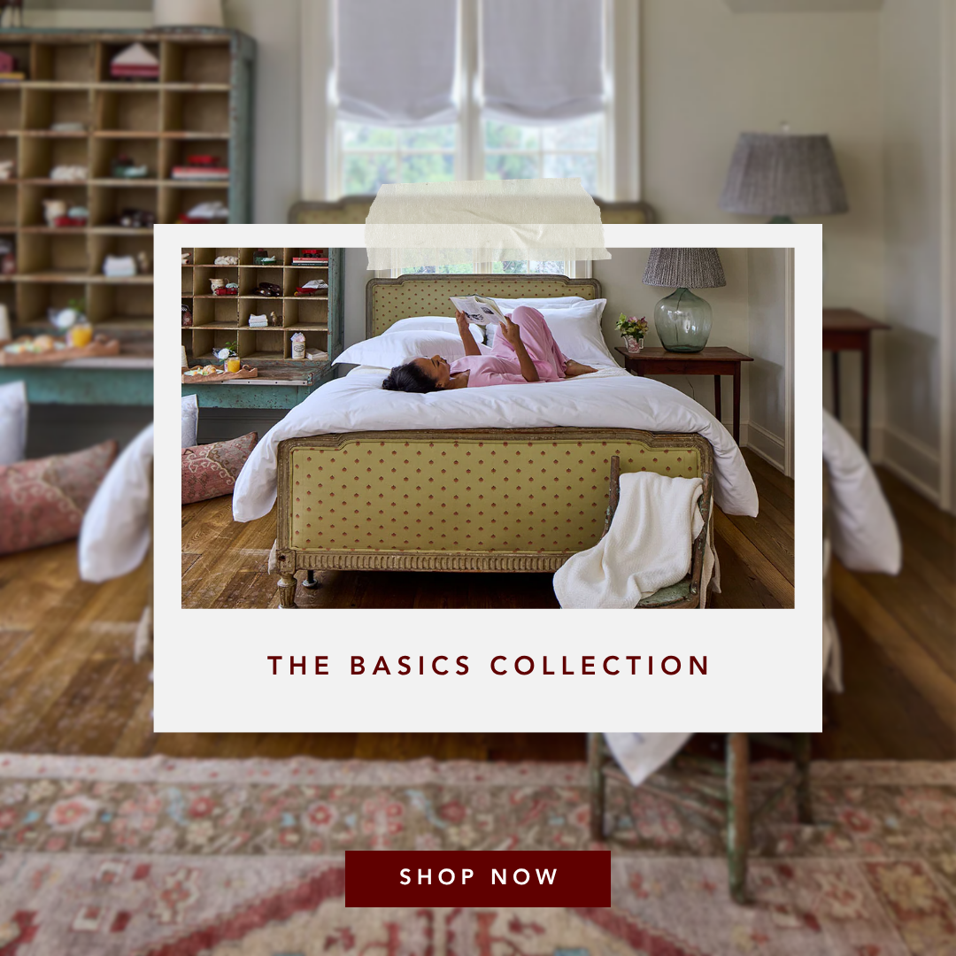 Woman in pink pajamas reading a book on a bed in a cozy bedroom.