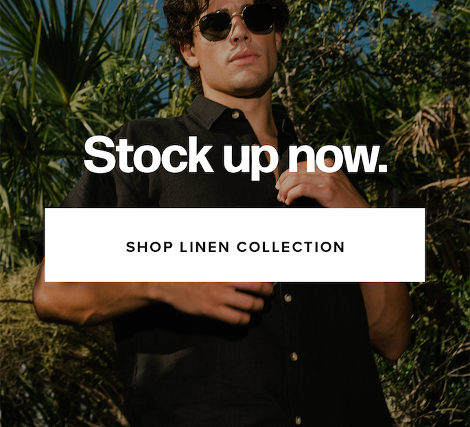 A close-up shows a man wearing sunglasses and a black short-sleeve button-down linen shirt against a backdrop of green palm trees and tropical plants. Text reads: 'Stock up now. Shop Linen Collection.'