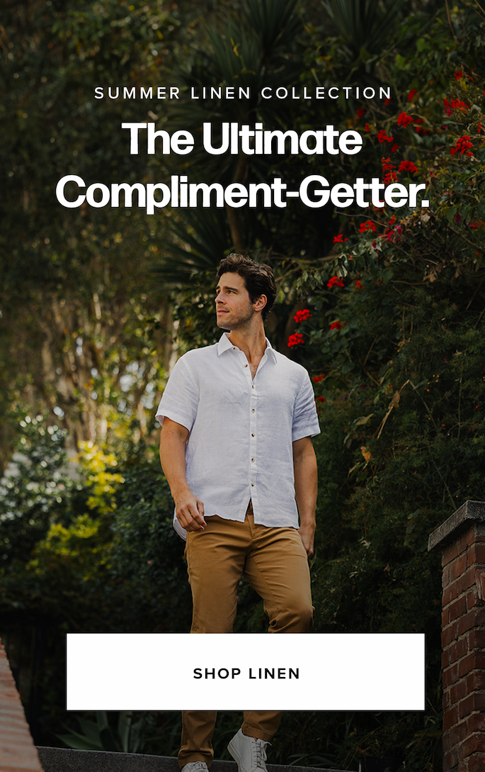 A man stands on outdoor steps wearing a white short-sleeve button-down shirt and tan pants. Lush green foliage and red flowers are behind him. Text reads: 'Summer Linen Collection. The Ultimate Compliment-Getter. Shop Linen.'