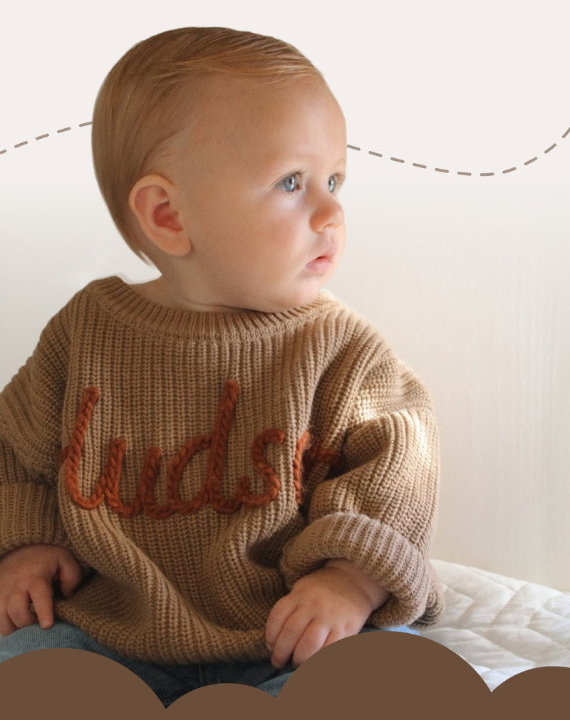 Baby wearing a personalized knit sweater while looking off to the side against a soft neutral nursery background.