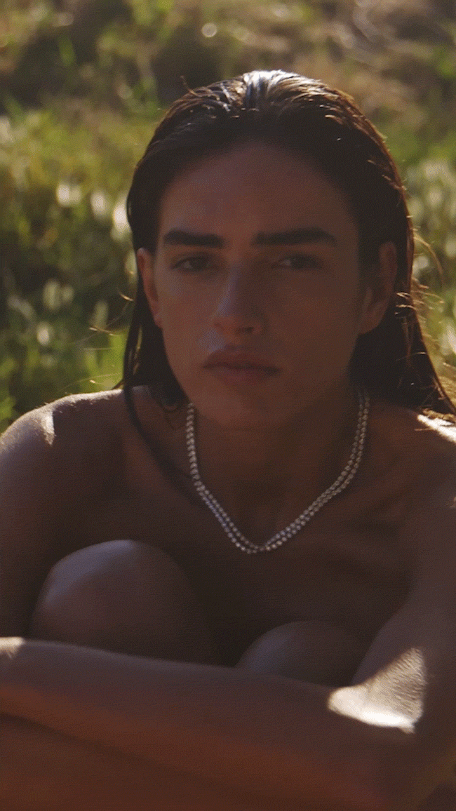 Animated GIF. A model sits in dappled sunlight wearing the Dorsey James Bezel Rivière Necklace.