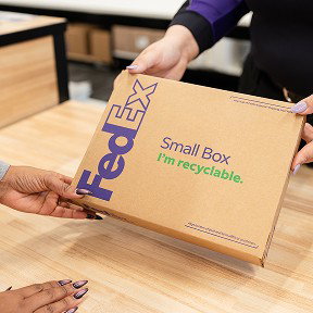 A FedEx Office employee hands a customer a shipping box.