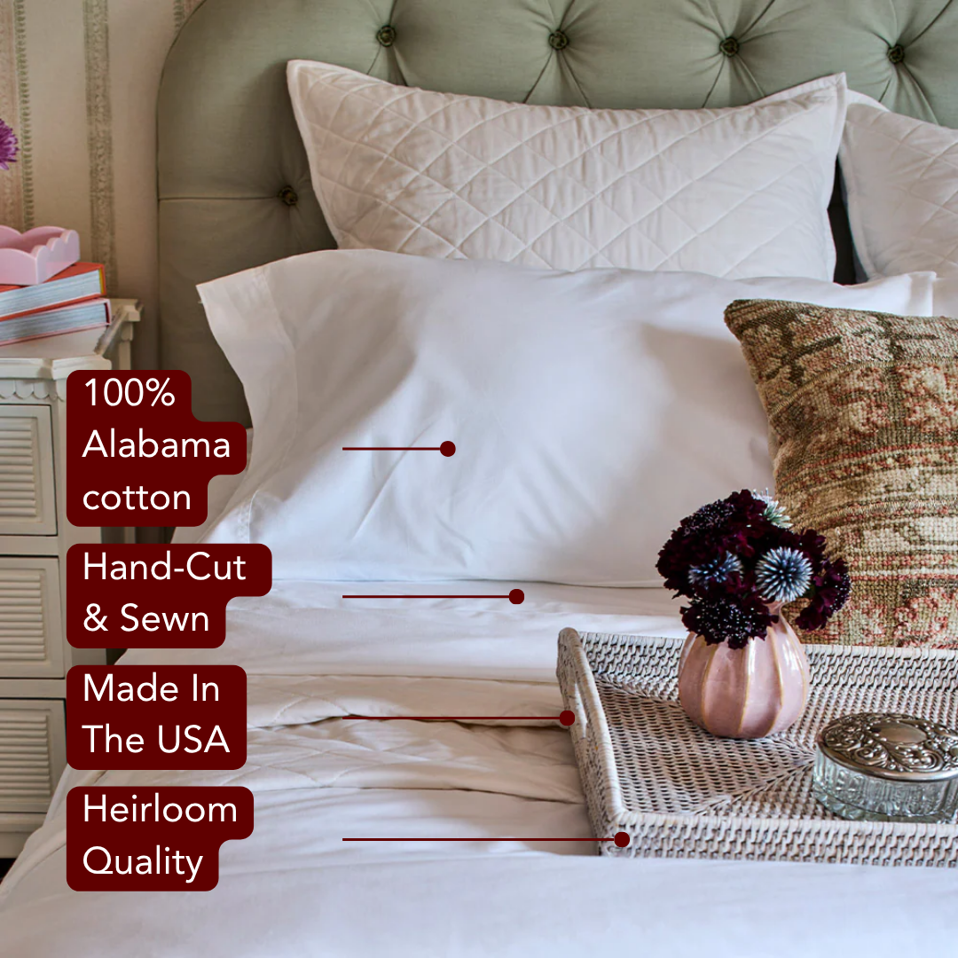 A close-up of a bed with white cotton pillows and sheets. A wicker tray with a vase of flowers rests on the bed. Text overlays list product features.