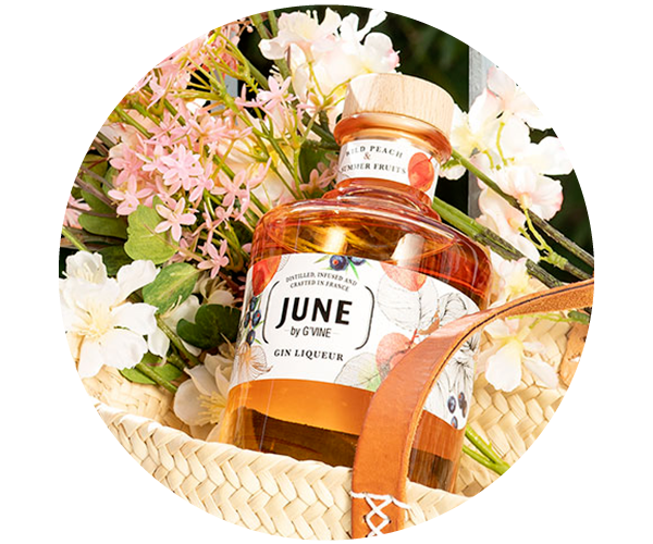 Bottle of June by G'Vine peach gin liqueur nestled in a woven picnic basket with pink and white flowers