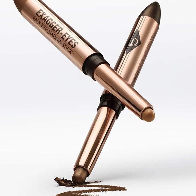 Two Charlotte TIlbury rose gold eyeshadow sticks, one open showing brown makeup, the other closed, arranged in a cross on a white background.