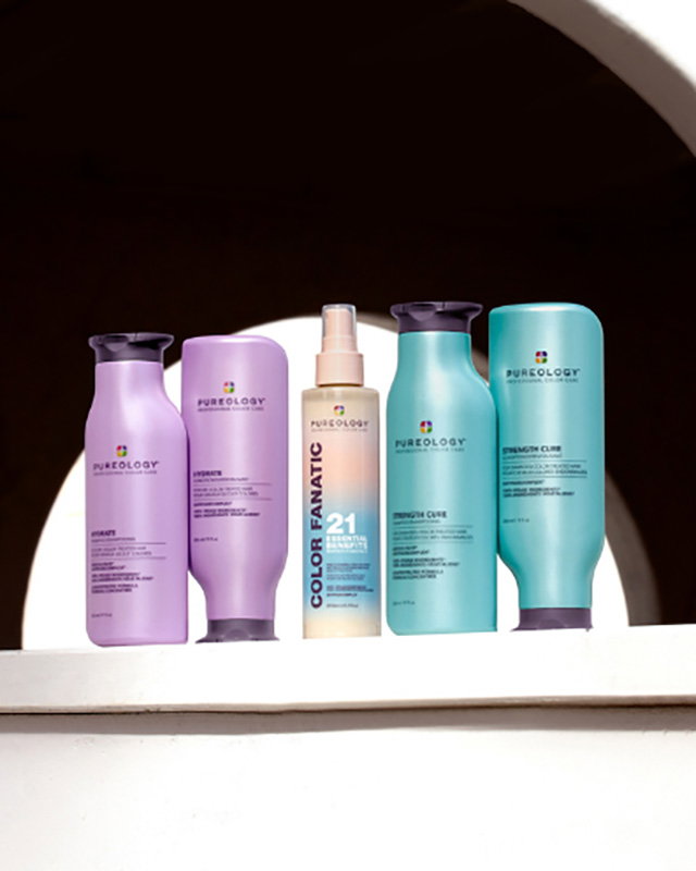 Various Pureology haircare products, including shampoos and a spray, are displayed in front of an archway.