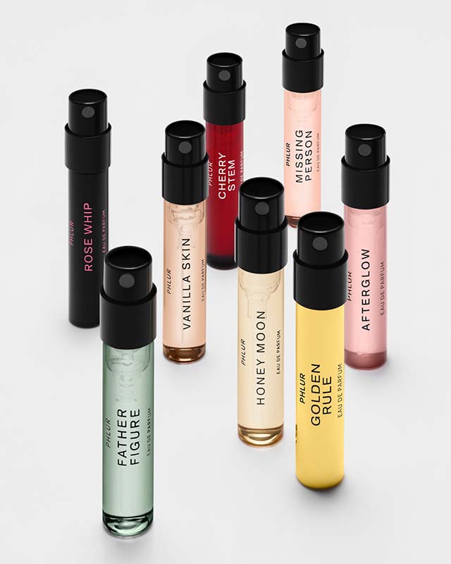 A collection of colorful Phlur perfume vials with black caps, each labeled with different fragrance names.