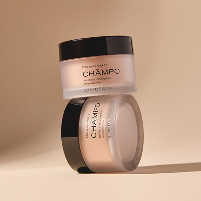 Two jars of CHAMPO hair repair mask with black lids, stacked on a neutral background.