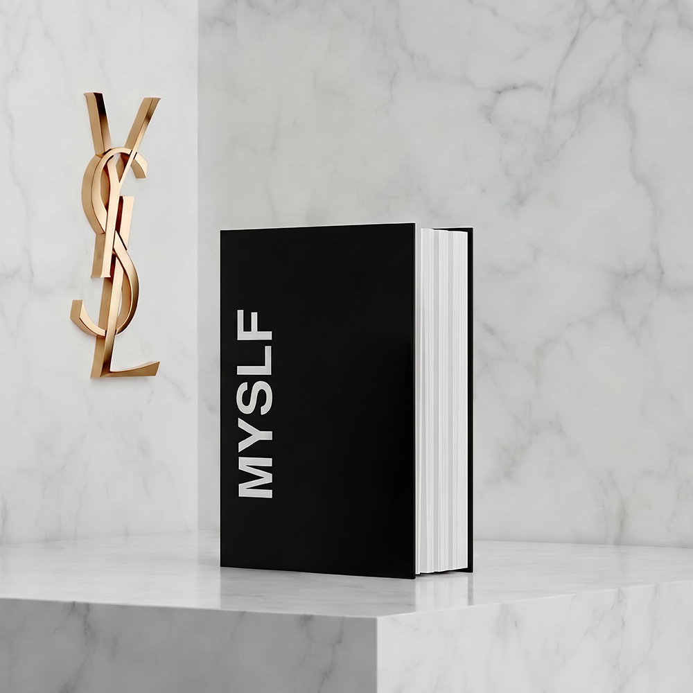 A black book titled "MYSLF" displayed on a white marble pedestal next to a golden YSL logo.