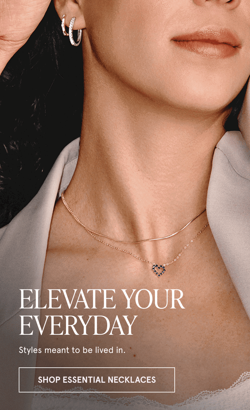 A model wearing diamond hoops and two gold necklaces. Elevate your everyday. Click here to shop essential necklaces