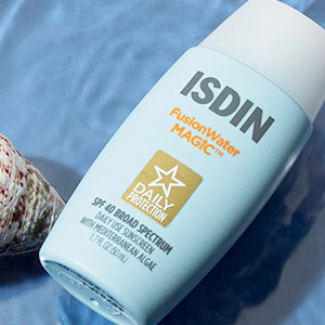 ISDIN bottle laying in water next to a white seashell