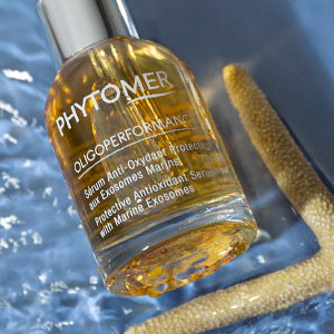 PHYTOMER glass serum bottle laying in glistening water next to a tan starfish