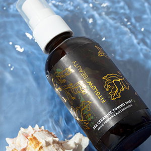 Fitglow Beauty spray bottle laying in rippling water next to a small conch shell
