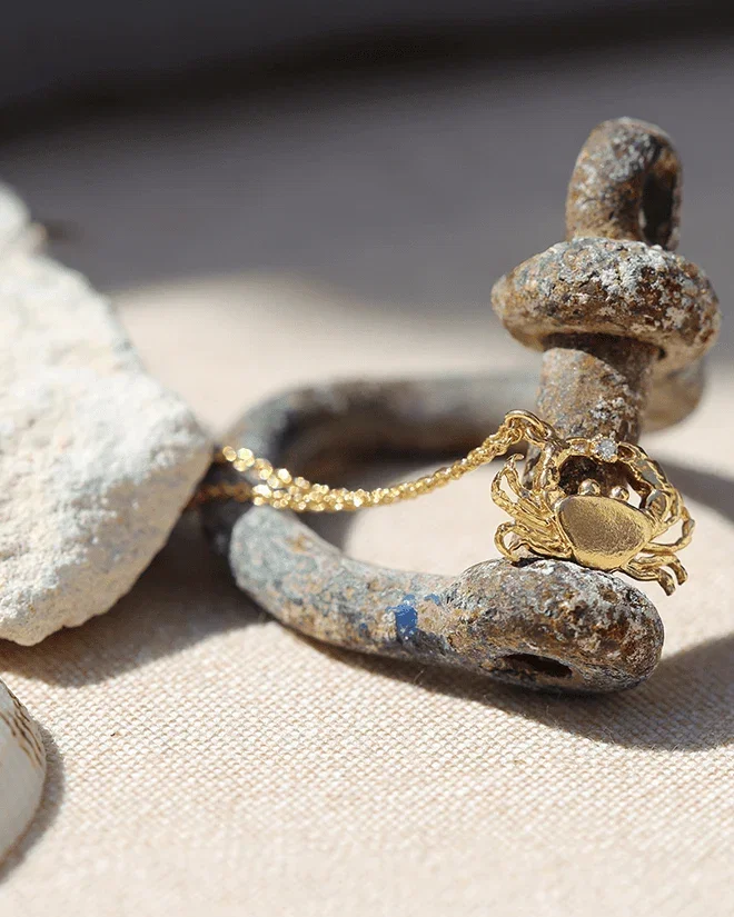 Teeny Tiny Crab Necklace draped over anchor on the beach