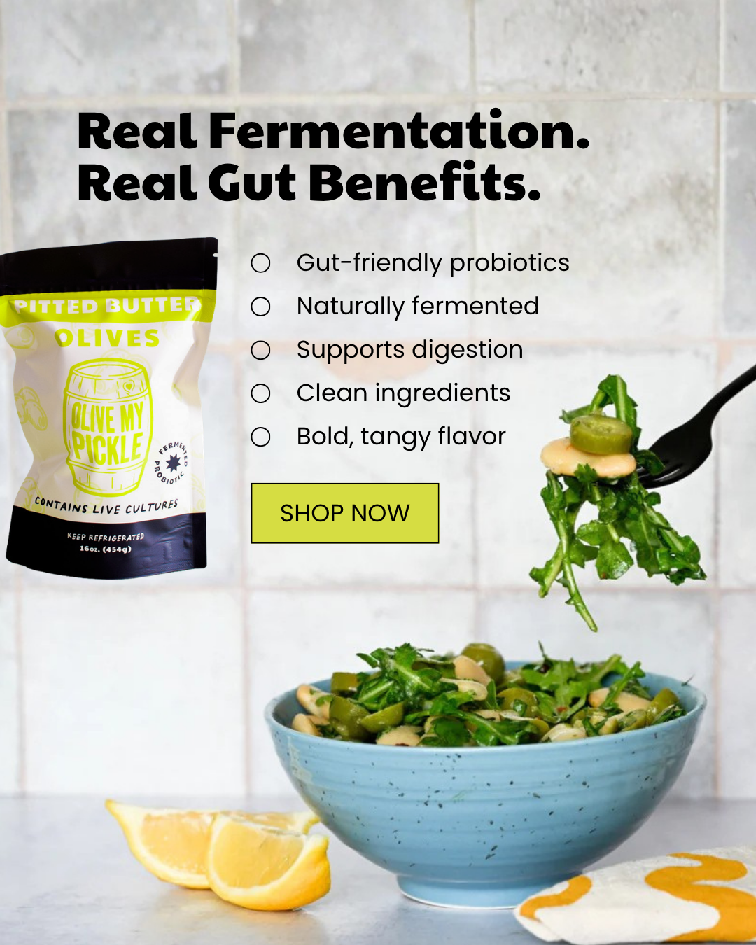 A bag of Olive My Pickle Pitted Butter Olives next to a blue bowl of olive and arugula salad. A fork lifts some salad. Text advertises 'Real Fermentation. Real
