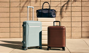 Three suitcases (one big, one medium-sized, and one small) with wheels arranged in front of a sunlit wall. A carry-on bag is on top of the big case.