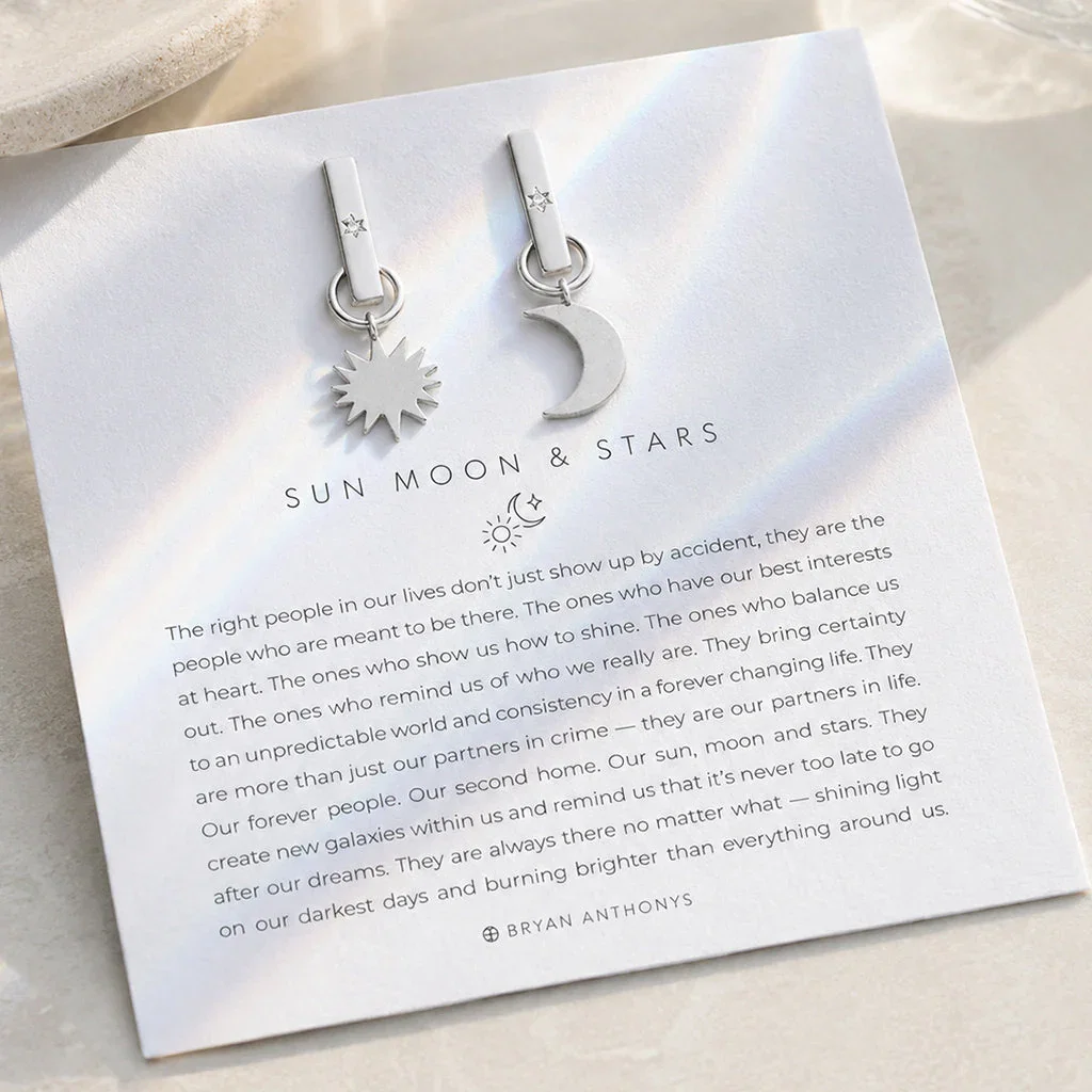 Silver sun and moon charm earrings displayed on 