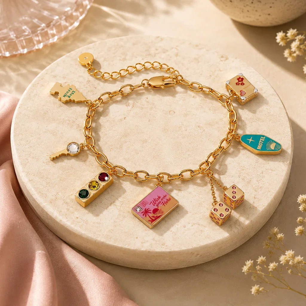 Gold charm bracelet with colorful enamel charms including dice, envelope, and turquoise pendant on cream plate.