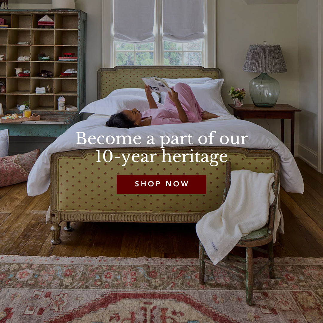 Woman reading on a patterned green bed in a cozy bedroom with an antique rug and shelving unit.