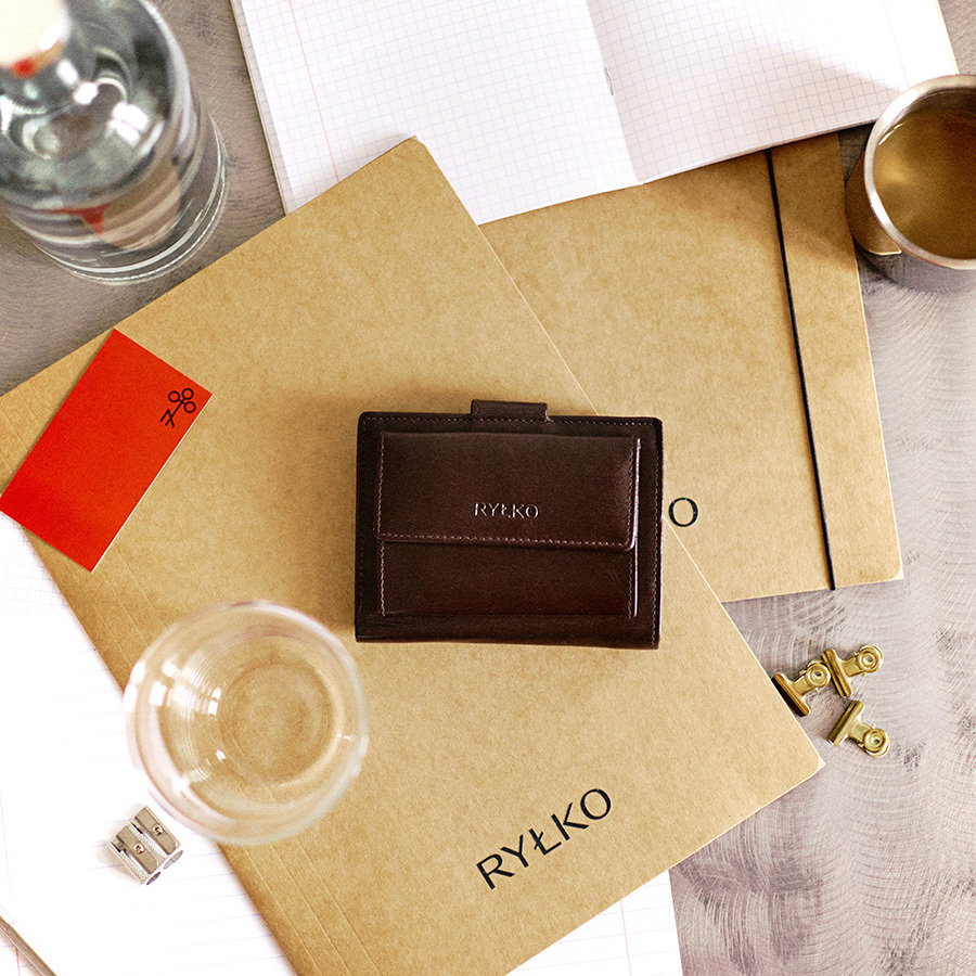 Brown leather wallet on Rylko notebooks with glass and stationery items.