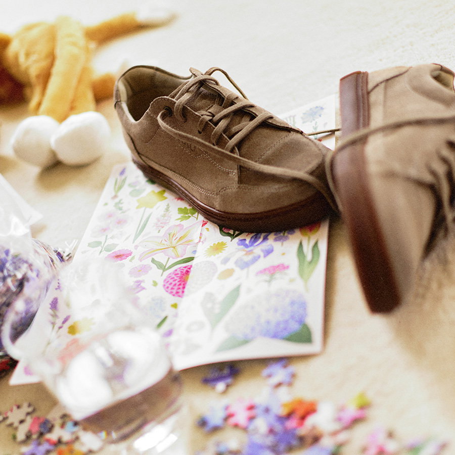 Brown suede shoes on floral paper with puzzle pieces and a soft toy in the background
