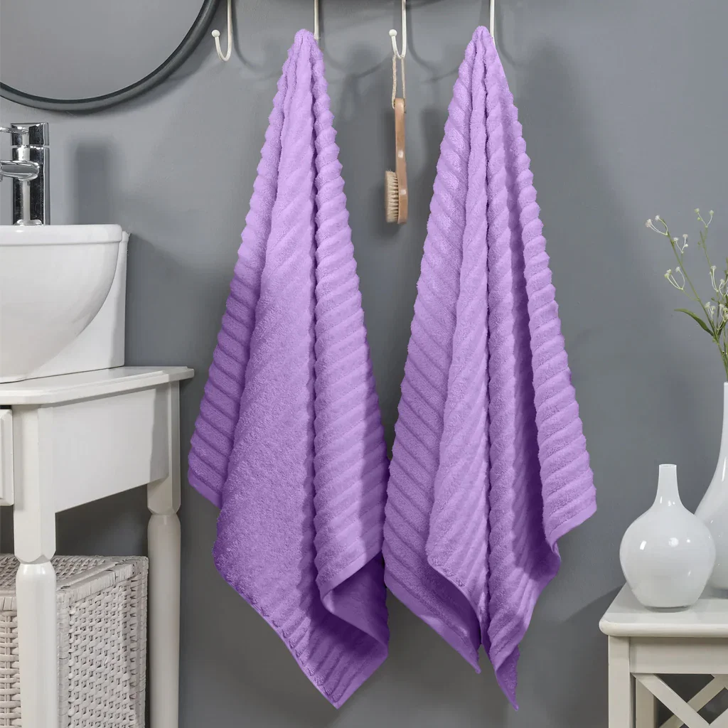 Two purple ribbed towels hanging in a modern bathroom with gray walls, white sink, and decorative white vase.