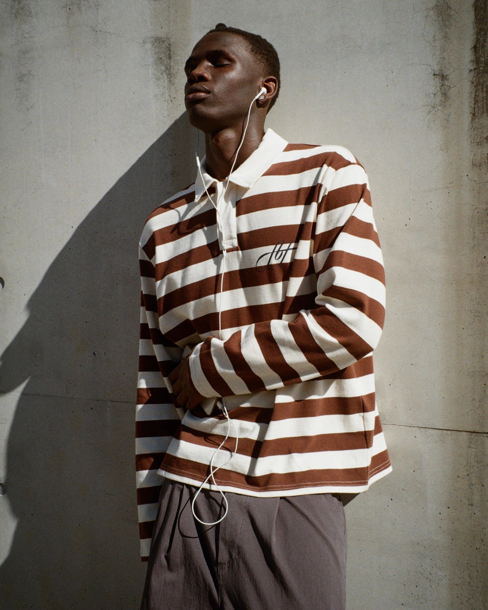 A medium shot captures a person with eyes closed wearing a brown and white horizontally striped long-sleeved polo shirt with a white collar and a logo...