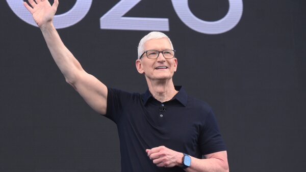 CEO Tim Cook waves during the annual World Wide Developers Conference at Apple's headquarters. He is wearing a black collared shirt and black framed glasses. 