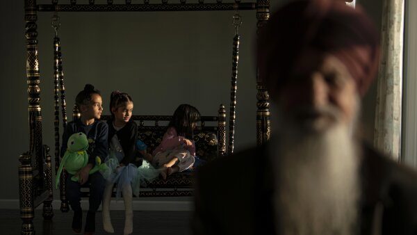 Agam Singh Brar, 7, plays with Kermit the Frog alongside his cousins behind his grandfather, who appears closer to the screen in a blur. 
