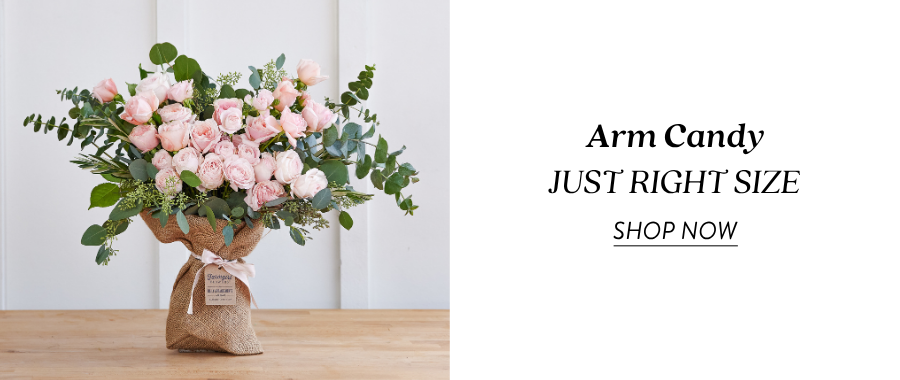 Product feature for “Arm Candy, Just Right Size,” showing a burlap-wrapped bouquet with pale pink roses, white flowers, and greenery on a wooden table. Text on the right reads “Arm Candy, Just Right Size” with a “Shop Now” link.