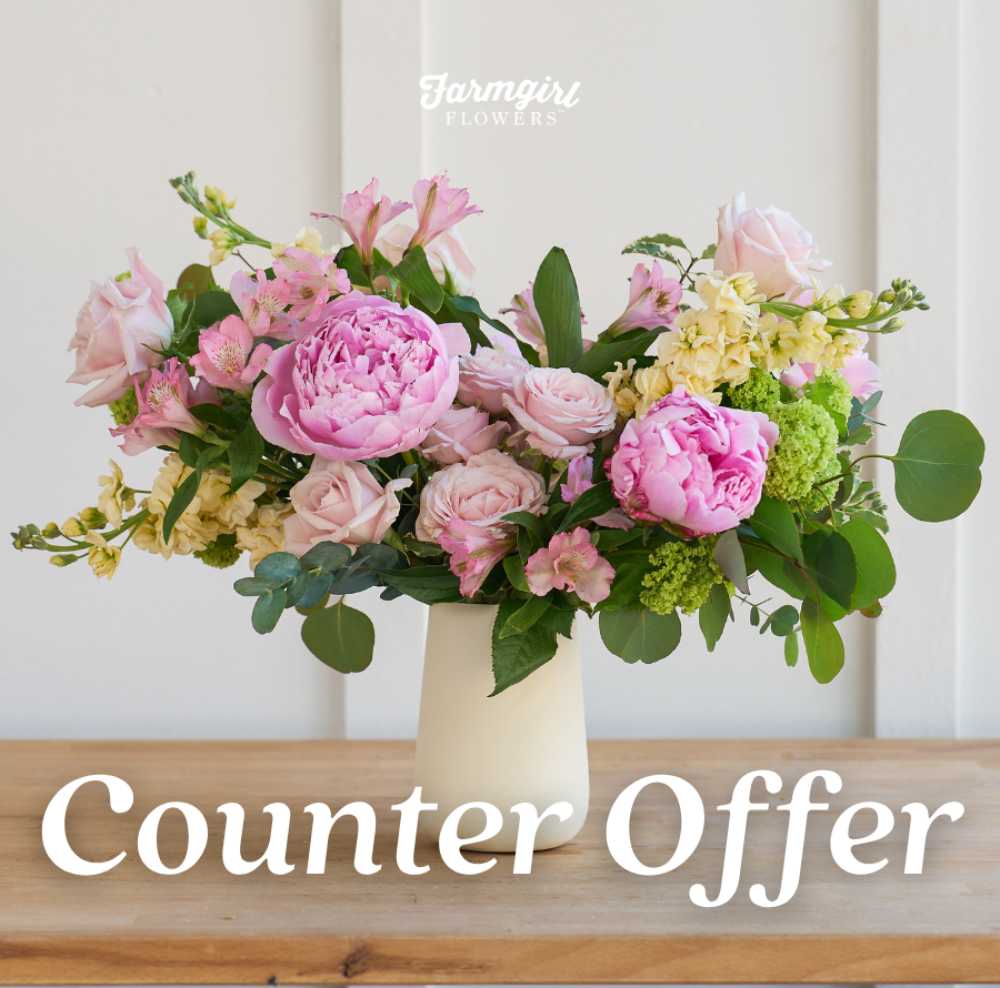 Farmgirl Flowers campaign image featuring a soft pink, blush, green, and white floral arrangement in a cream vase on a wooden table. White text reads “Counter Offer,” with the Farmgirl Flowers logo near the top.